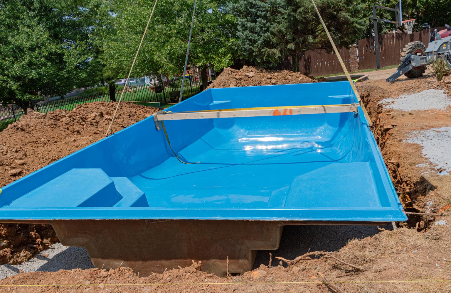 Blue fiberglass inground swimming pool being lowered into an excavated backyard hole